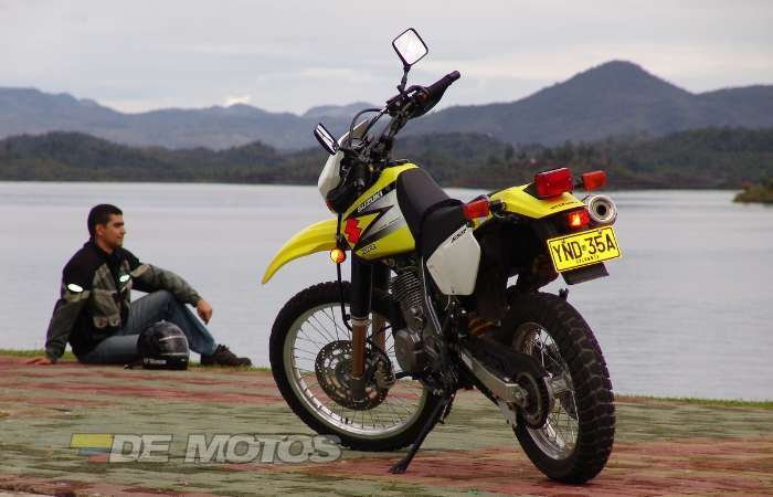 Foto de la Suzuki DR 650 de color amarillo y blanco estacionada al pie de un lago