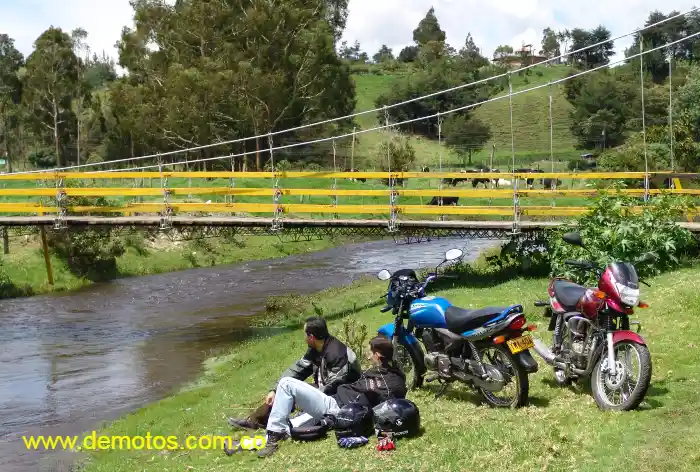 Paisaje de motociclistas en el campo y al lado las Kawasaki Wind 125 en color azul y vino tinto estacionadas